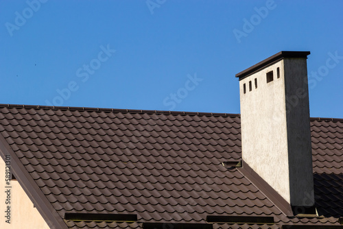 Roof of a new home. Ceramic chimney, metal roof tiles, gutters, roof window. Single family house
