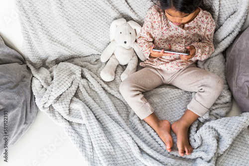 Girl (4-5) sitting on sofa and looking at smart phone
