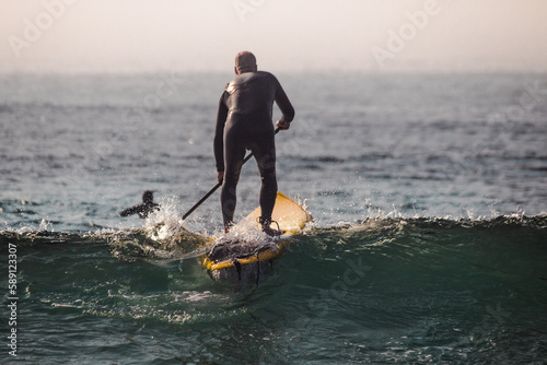 A man doing Stand up paddle on the beach while there are waves at sunset 