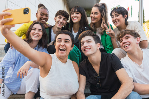 Multiethnic group of happy young friends sitting on stairs taking selfie - Diverse teenagers having fun while a break of university classes
