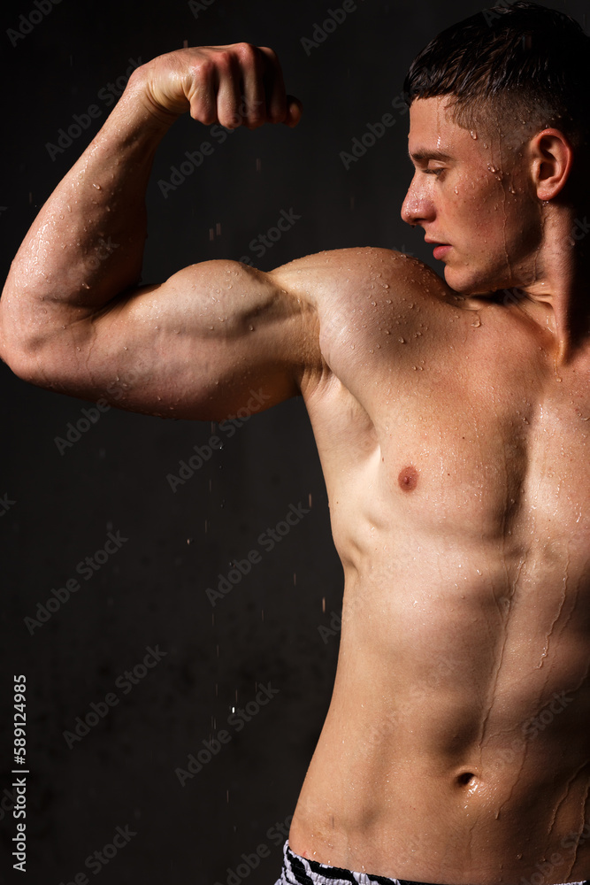 Fototapeta premium Athlete bodybuilder trains in the studio in the rain.