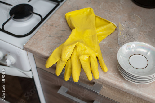 Kitchen composition of rubber yellow gloves and a set of plates on the nightstand, in the kitchen. An image about housework, apartment care and cleanliness.