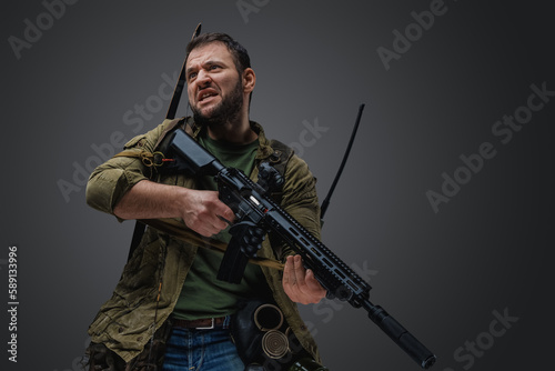 Studio shot of isolated on grey background aggressive man with rifle survived after armageddon.