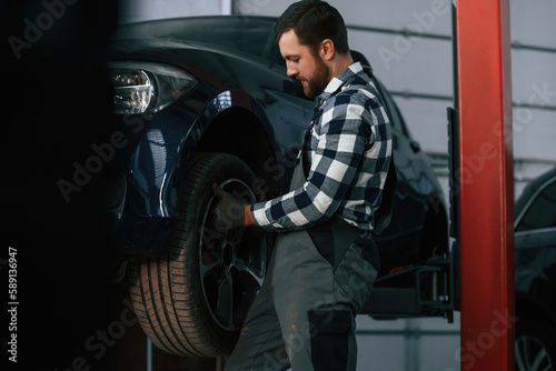 Holding and changing new tire. Man in uniform is working in the auto salon © standret