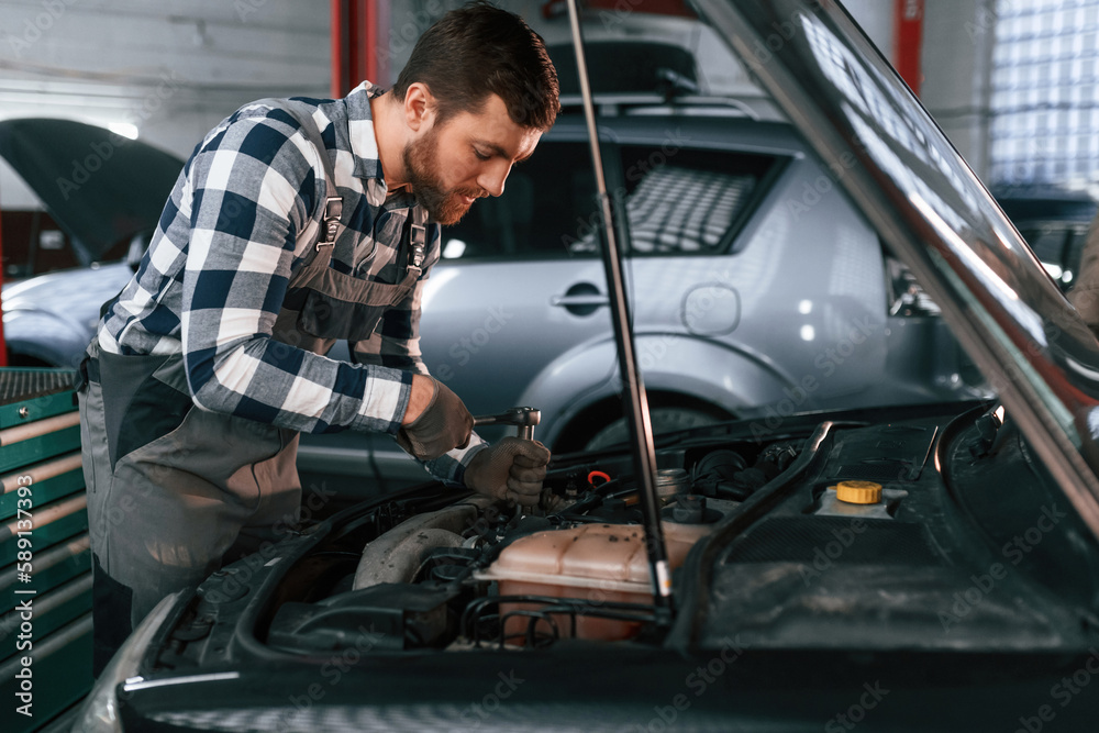 Repairing the electronics of the car under the hood. Man in uniform is working in the auto salon Repairing the electronics of the car under the hood. Man in uniform is working in the auto salon