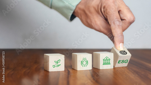 ESG concept of environmental, social and governance. Sustainable corporation development. Hand flips wooden cubes with target setting to ESG icon with other ESG icons on bright background.Copy space