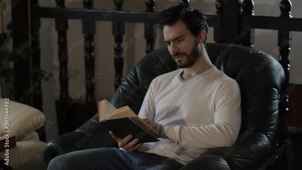 Bearded Middle Aged Man Reading a Book Indoors on an Armchair Bearded Middle Aged Man Reading a Book Indoors on an Armchair