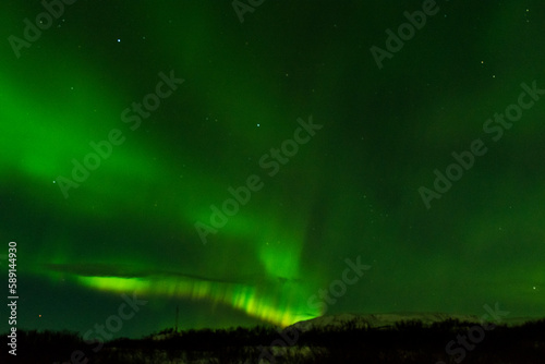 imagen de un paisaje nocturno nevado, con montañas de fondo, y una aurora boreal sobre el cielo de Islandia 