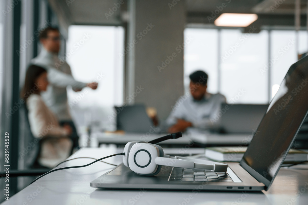 Fototapeta premium Headphones is lying down on the laptop. Men and woman are working in the office together