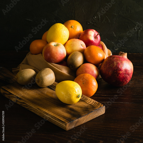 Fruit in a reusable bag. Earth day and zero waste concept. Orange, lemon, apple, kiwi, pomegranate and wooden cutting board on dark background