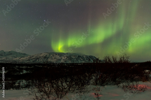 imagen de un paisaje nocturno nevado  con monta  as de fondo  y una aurora boreal sobre el cielo de Islandia 
