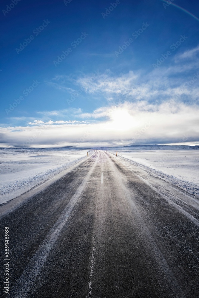 Long empty road surrounded by snow-covered fields on a sunny day in Iceland Long empty road surrounded by snow-covered fields on a sunny day in Iceland