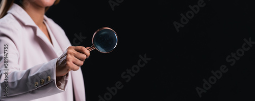Business woman hand holding magnifier for inspection on black background