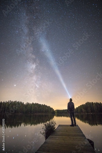 Vertical shot of a person standing on a boardwalk admiring the Milky Way and the starry night