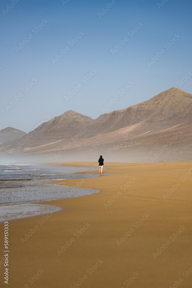 Stunning view a person walking on the Cofete beach surrounded by the chain of mountains of the Jandía Natural Park. Fuerteventura, Canary Islands.
