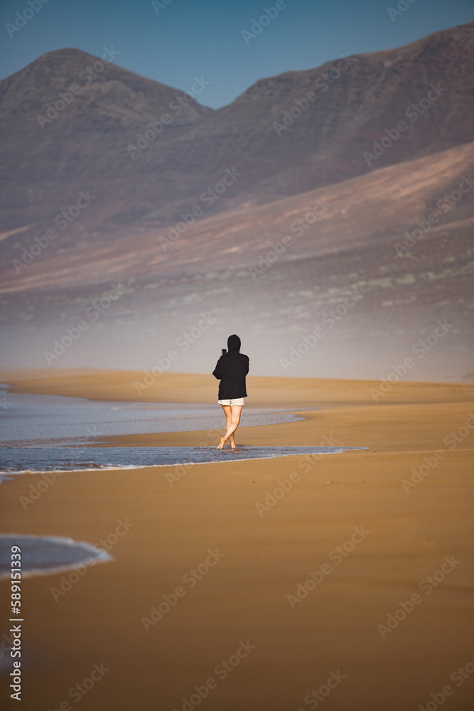 Stunning view a person walking on the Cofete beach surrounded by the chain of mountains of the Jandía Natural Park. Fuerteventura, Canary Islands.