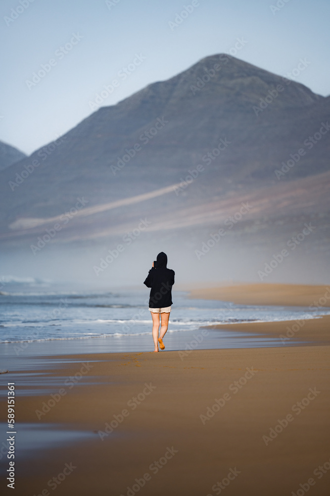 Stunning view a person walking on the Cofete beach surrounded by the chain of mountains of the Jandía Natural Park. Fuerteventura, Canary Islands.