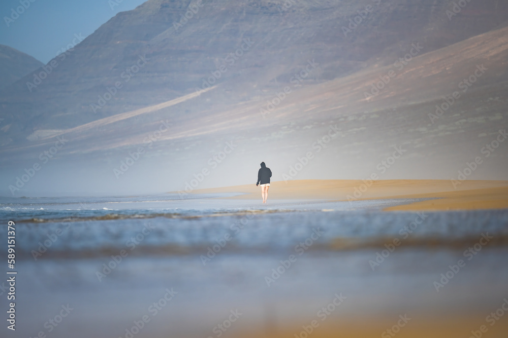 Stunning view a person walking on the Cofete beach surrounded by the chain of mountains of the Jandía Natural Park. Fuerteventura, Canary Islands.