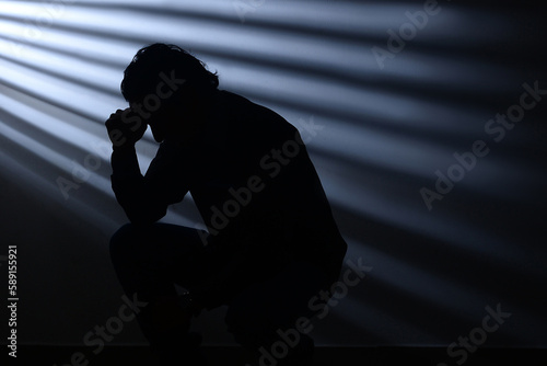 Silhouette of a desolate man bent over on his feet against a background of light rays. Mysterious and enigmatic mood. Despair