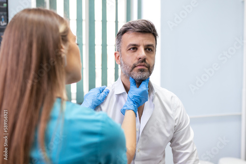 medicine, healthcare and medical exam concept - doctor or nurse checking patient's tonsils at hospital. Endocrinologist examining throat of young man in clinic