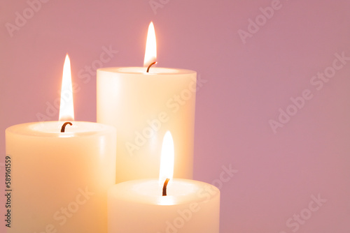 Close up of scented white candles melting and burning on pink background. Copy space for text. 