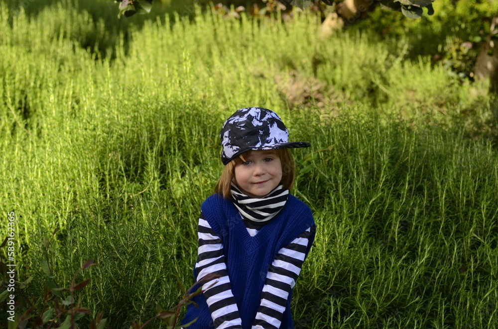 Positive boy fooling around. Cute baby on a walk in the park. Portrait of a boy 4 years old in a striped jacket and cap Positive boy fooling around. Cute baby on a walk in the park. Portrait of a boy 4 years old in a striped jacket and cap