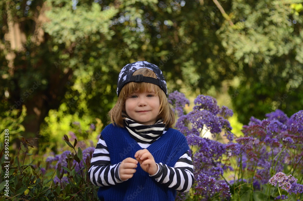 Positive boy fooling around. Cute baby on a walk in the park. Portrait of a boy 4 years old in a striped jacket and cap Positive boy fooling around. Cute baby on a walk in the park. Portrait of a boy 4 years old in a striped jacket and cap