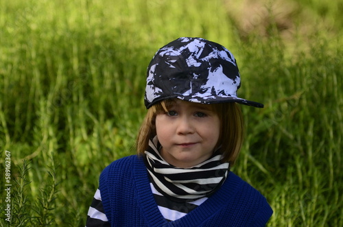 Positive boy fooling around. Cute baby on a walk in the park. Portrait of a boy 4 years old in a striped jacket and cap