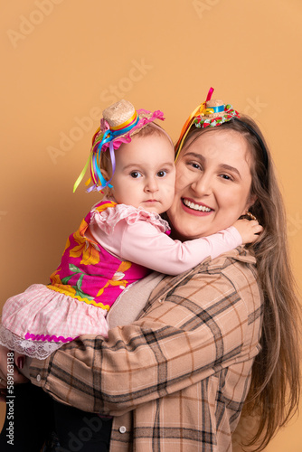 fun baby girl and mom to Brazilian Junina Festival in beige background. hugging each other 