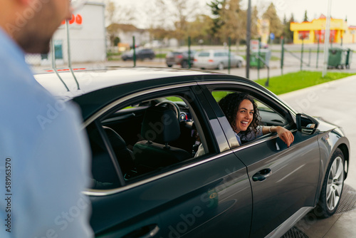 The husband pours fuel into the tank while the wife sits in the passenger seat and laughs © DusanJelicic