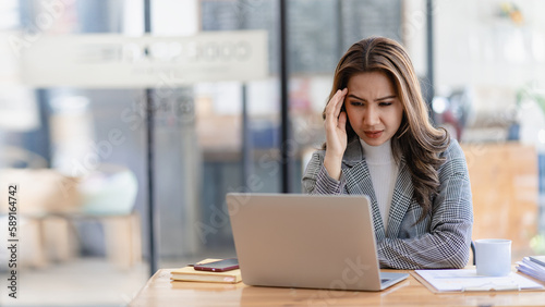 Fotografie Stressed and frustrated asian female accountant sitting at desk making serious b