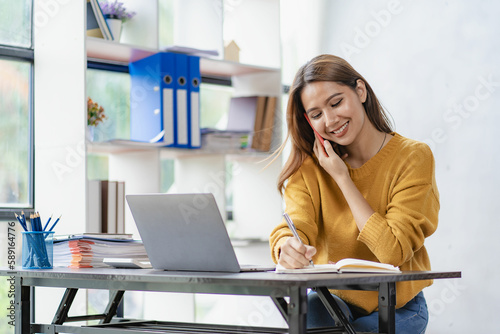 Asian businesswoman using smartphone to start online delivery Freelancer or salesman checking production order with laptop. SME entrepreneur working with parcel box at home.
