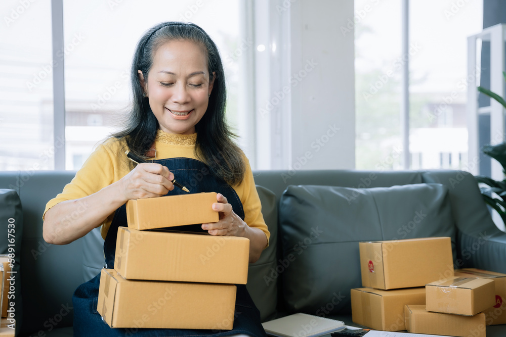 woman start up small business owner writing address on cardboard box at workplace.small business entrepreneur SME or freelance asian woman working with box at home. woman start up small business owner writing address on cardboard box at workplace.small business entrepreneur SME or freelance asian woman working with box at home.