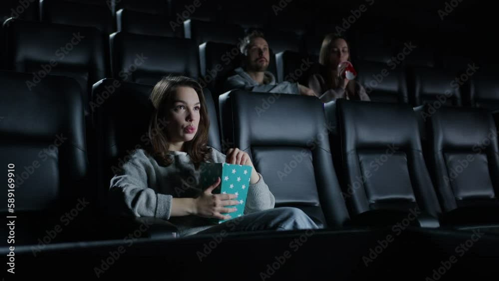 Evening movie screening. People in the cinema are watching a movie. In the foreground is a woman eating popcorn Evening movie screening. People in the cinema are watching a movie. In the foreground is a woman eating popcorn