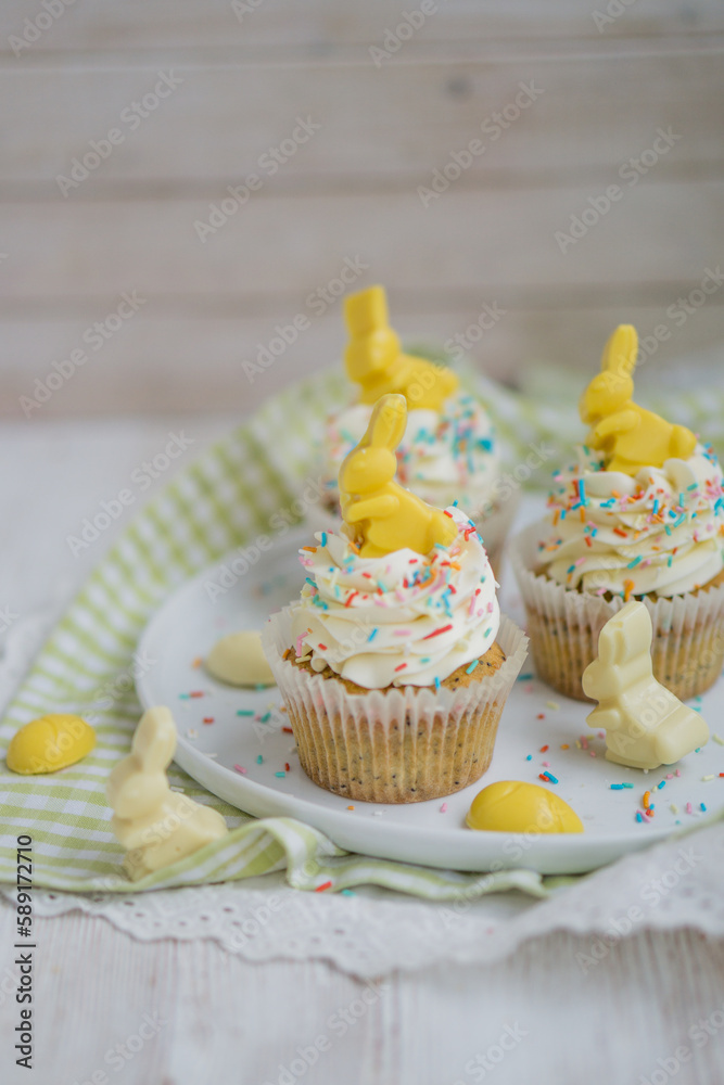 Lemon poppy seeds cupcakes with white whipped buttercream and white and yellow chocolate bunnies and coloreful sprinkles easter baking close up selective focus