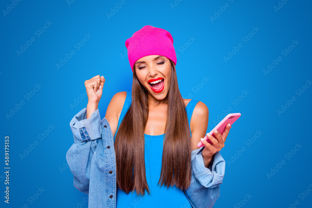 Charming and happy girl joyfully clasps her hand in a fist and holding the phone in her hands isolated on bright pink background Charming and happy girl joyfully clasps her hand in a fist and holding the phone in her hands isolated on bright pink background