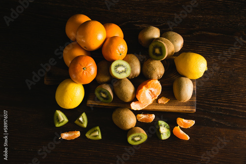 Flatlay, sweet fruit on a dark background. Tangerines, lemons, kiwis, whole fruits and pieces on a wooden cutting board