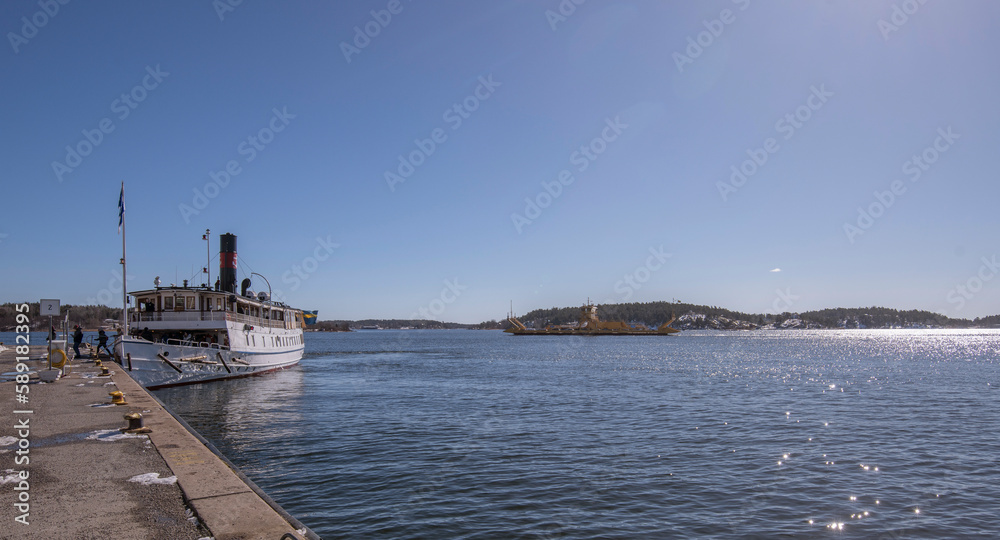 Old steam ship at the jetty in the archipelago town Vaxholm, an Trafikverkets yellow road ferry in background passing. a sunny spring day in Stockholm