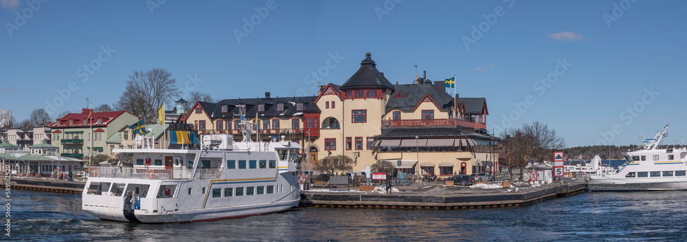 Commuter archipelago ferries in the bay at the archipelago town Vaxholm, famous fortress and hotel, a sunny spring day in Stockholm