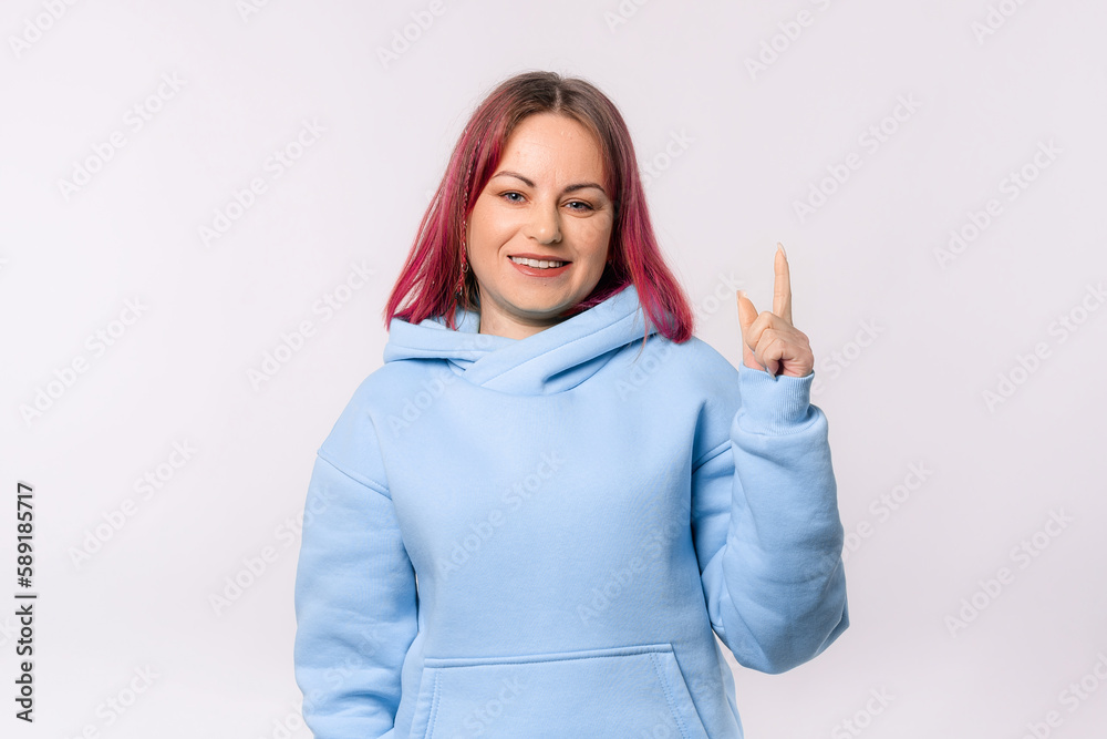 Portrait of pretty smiling young woman with pink hair pointing finger up, showing advertisement, company banner on top Portrait of pretty smiling young woman with pink hair pointing finger up, showing advertisement, company banner on top