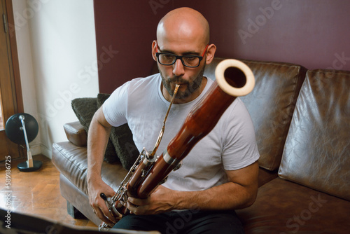 front view of young classical music composer man, playing bassoon reading sheet music at home photo