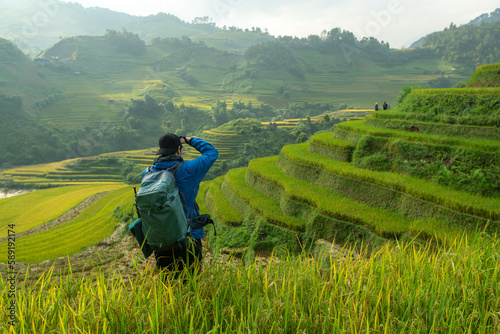 Tourist is standing on the viewpoint and take picture of rice terraces scenery at Mu Cang Chai in the north of Vietnam.