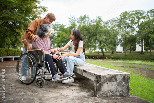 Asian careful caregiver or nurse taking care of the patient is hurting knee in wheelchair. Concept of happy retirement with care from caregiver and Savings and senior health insurance, a Happy family