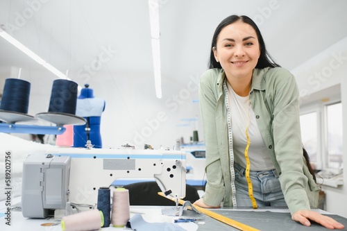 Happy female dressmaker working with sewing machine at textile factory.