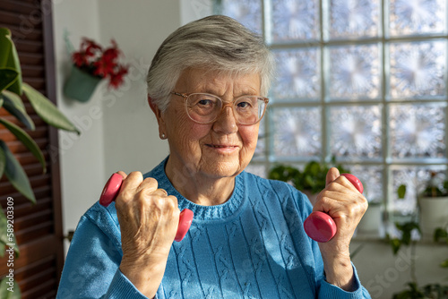 85 years old senior woman doing sport with dumbbells in winter garden 