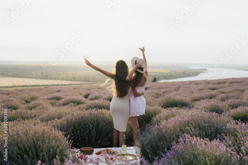Two beautiful young girlfriend drinking wine on picnic  having fun and watching the sunset. Summer travel concept.