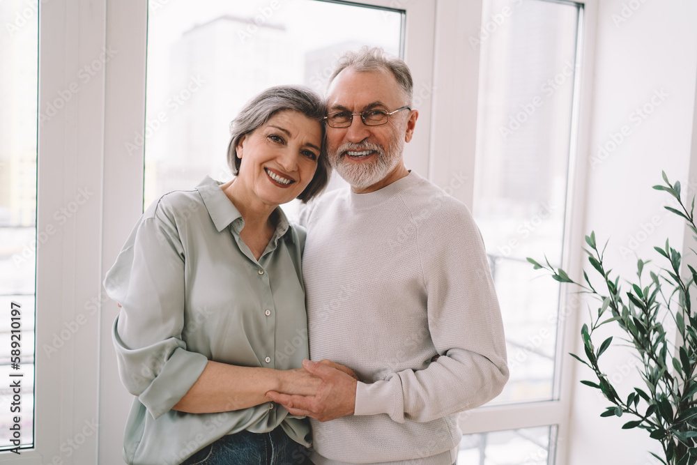 Fototapeta premium Happy senior couple hugging at home and looking at camera