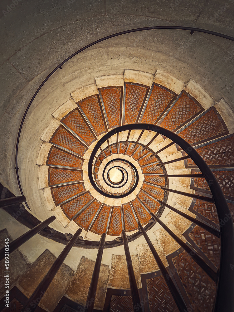 Circular staircase with black metal railing, inside the triumphal arch, Paris, France. Abstract background, a look downstairs an infinite swirl stairway