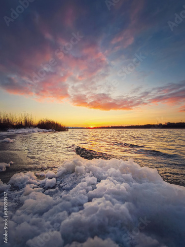 Windy evening at the lake with waves creating white foam on the shore. Vibrant sunset scene over the pond