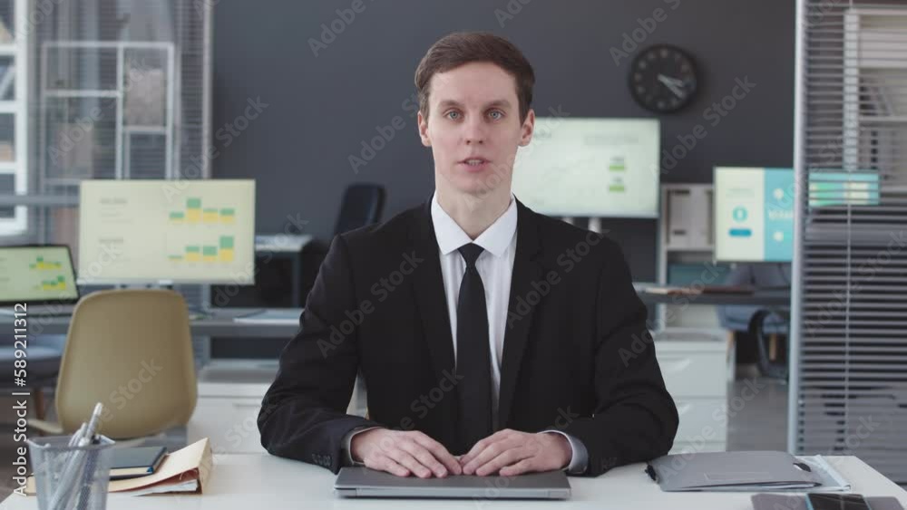 Waist up POV of Caucasian male financial consultant speaking at camera sitting at desk in modern office Waist up POV of Caucasian male financial consultant speaking at camera sitting at desk in modern office